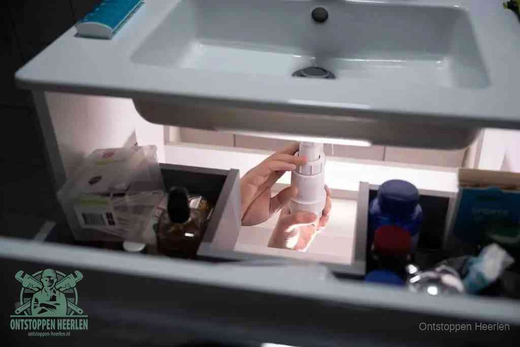 Een pompfles met zeep boven een wastafel, de heet water en afwasmiddel-methode om een vetprop in de afvoer los te maken in Heerlen