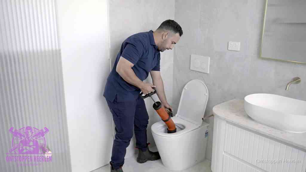 Een monteur buigt over een wandcloset en duwt met de hand een persluchtontstopper in de toiletpot om de verstopping handmatig los te maken in Heerlen