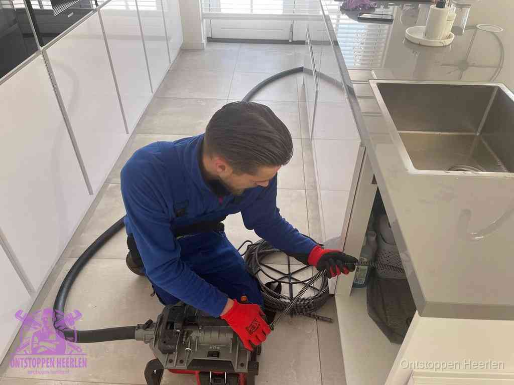 Een monteur ontstopt de keukenafvoer onder de spoelbak met een elektrische veermachine in Heerlen