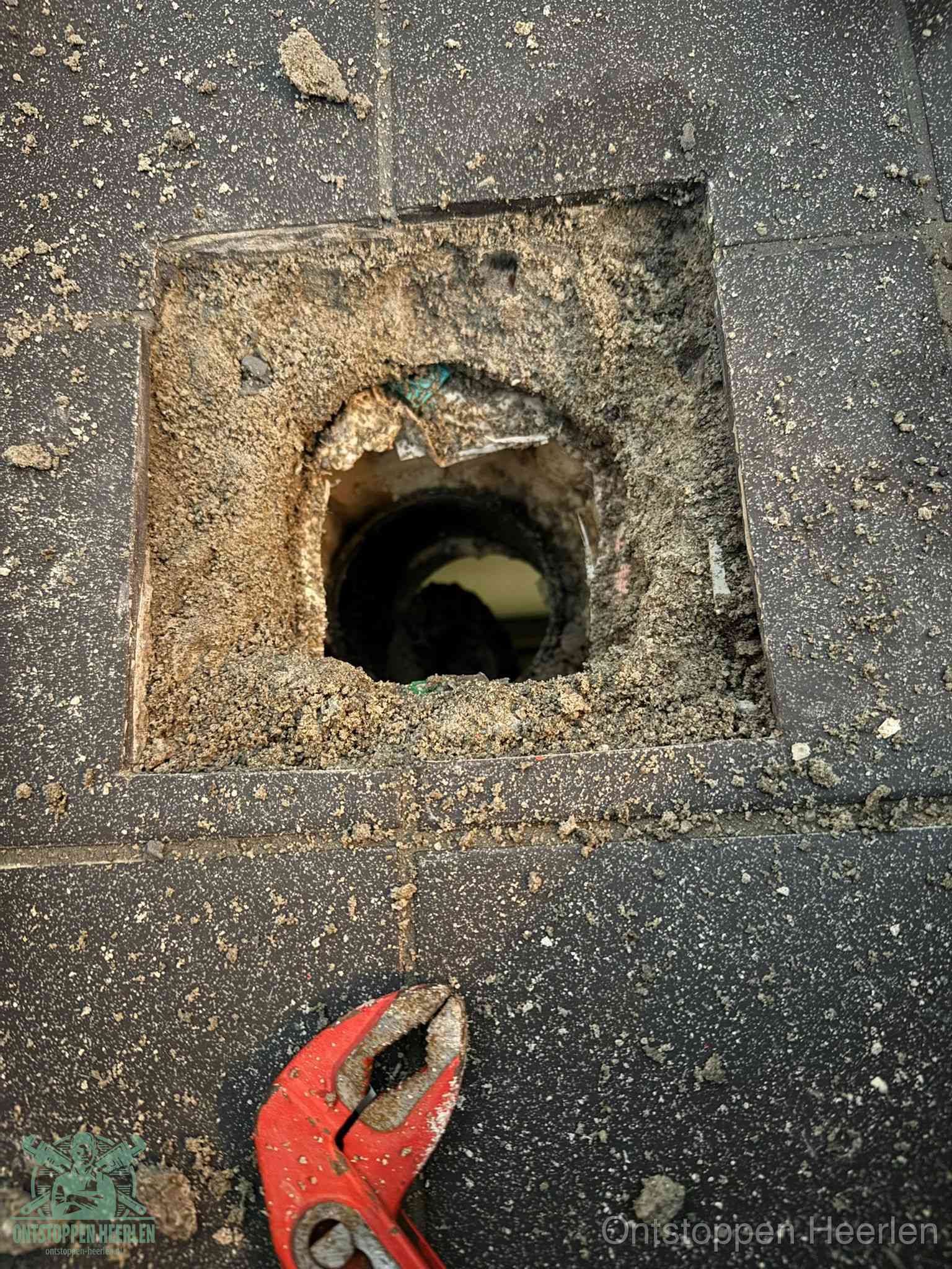 Een geopend rioolputje in een betontegelvloer met losgemaakt rooster en een zichtbare ronde afvoerbuis, het achterhalen waar de afvoerverstopping zit in Heerlen
