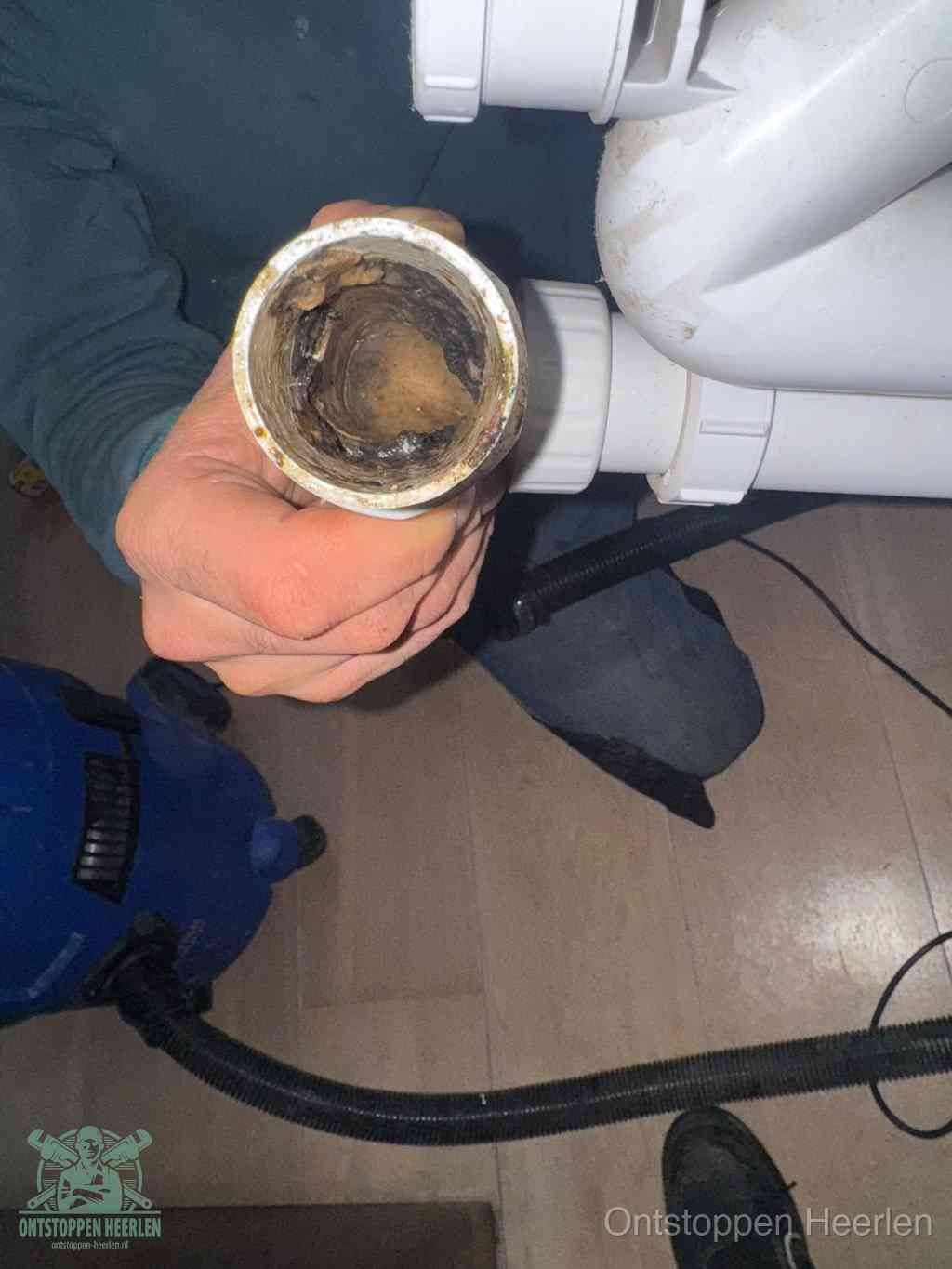 Een hand houdt een losgekoppeld PVC-afvoerbuisstuk vast dat van binnen volledig is dichtgeslibd met vet, vuil en aanslag, de meest voorkomende oorzaak van een verstopte afvoer in Heerlen