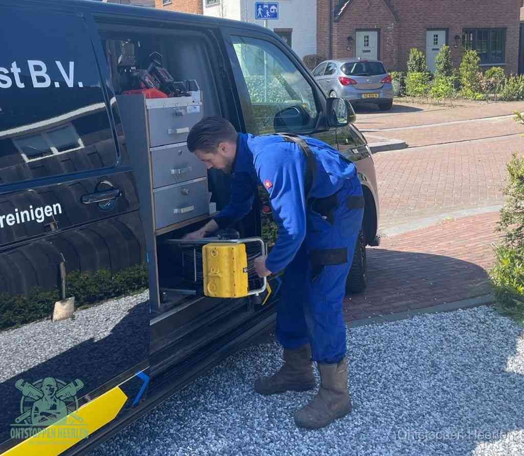 Een monteur pakt buiten op de oprit gereedschap uit de bedrijfsbus, het moment om een professional in te schakelen voor een verstopte afvoer in Heerlen