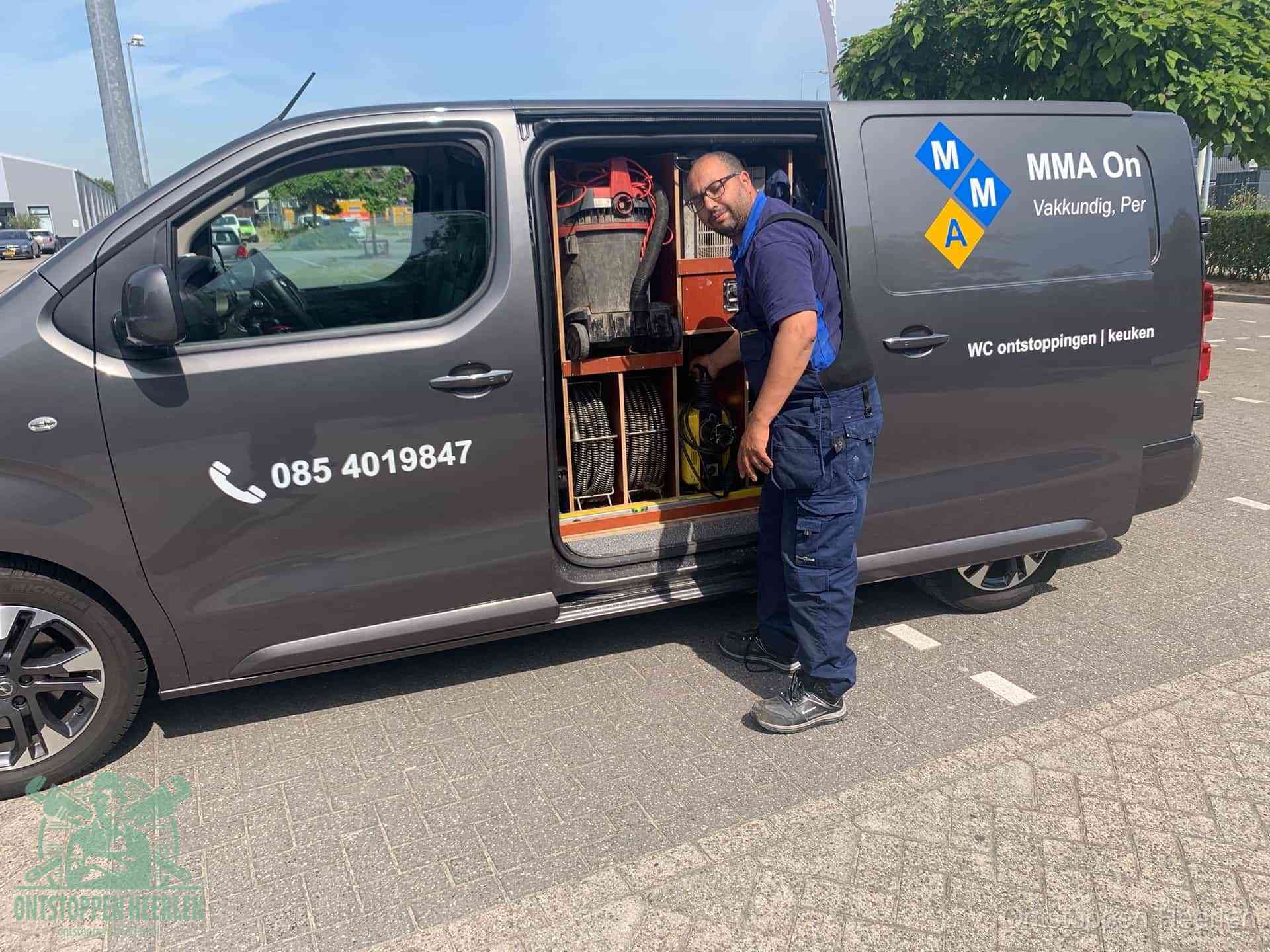 Een monteur bij de open schuifdeur van zijn bedrijfsbus op een parkeerplaats, klaar om de oorzaak van terugkerende afvoerverstoppingen aan te pakken in Heerlen
