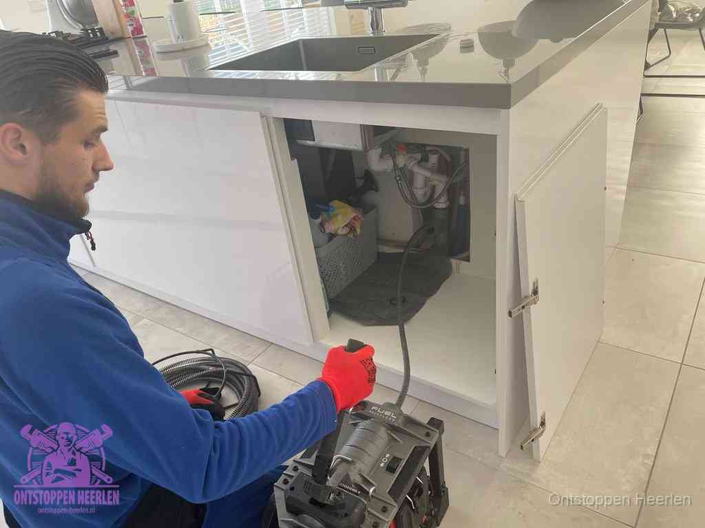 Monteur ontstopt met een veermachine een verstopte afvoer onder de gootsteen in Heerlen