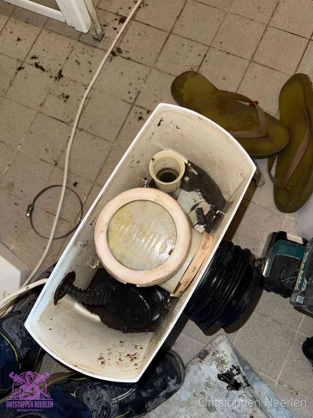 Een gedemonteerde toiletpot op de vloer met ontstoppingsveer en gereedschap ernaast, het verwijderen van een vastzittend voorwerp uit de wc in Heerlen