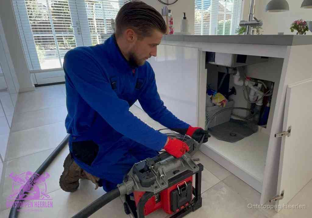 Een monteur voert een professionele elektrische ontstoppingsmachine in de afvoer onder de spoelbak tijdens het gootsteen ontstoppen in Heerlen